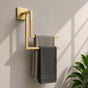 Gold wall mounted staggered towel rack holding gray towels on a bathroom wall.