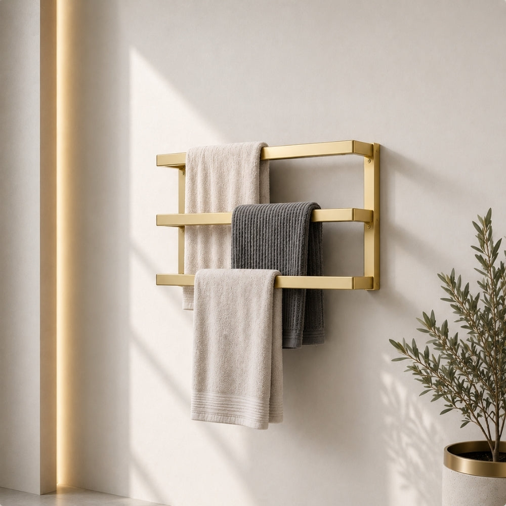 Gold wall mounted triple towel bar rack holding three towels on a light bathroom wall.