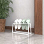 A white metal slipper holder showcasing a minimalist design, holding white and mint-green slippers, placed near a wooden trim and potted plant