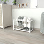A sleek white metal slipper stand on a wooden floor near a white cabinet and decorative accents, holding multiple pairs of gray and white slippers