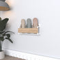A white wall-mounted slipper rack with a wooden front, designed for compact and elegant storage, holding three pairs of slippers in soft pastel tones